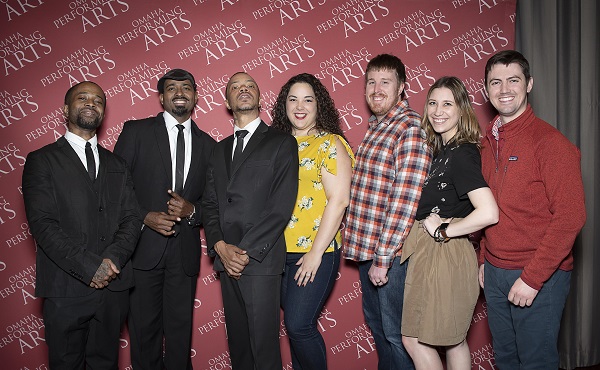 Members of 40 Below post with members of the Hypnotic Brass Ensemble in front of an OPA backdrop after a show.