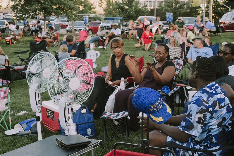 Two women sit in front of fans in the park