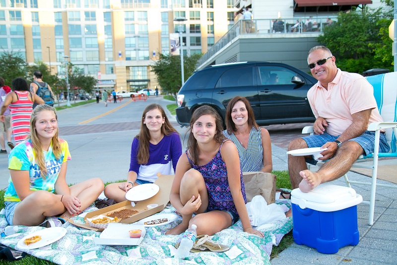 A family sits in the park on a blanket with chairs and a cooler